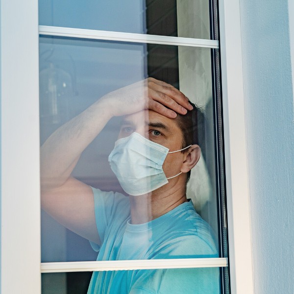 Mann mit Mund-Nasen-Schutz blickt aus dem Fenster_Bildquelle: DimaSid/shutterstock.com