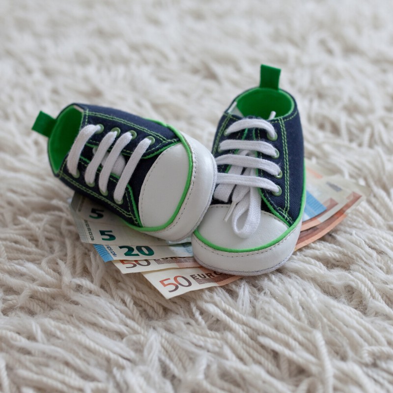 Babyschuhe stehen auf Geldscheinen / Credit: bpstocks/AdobeStock
