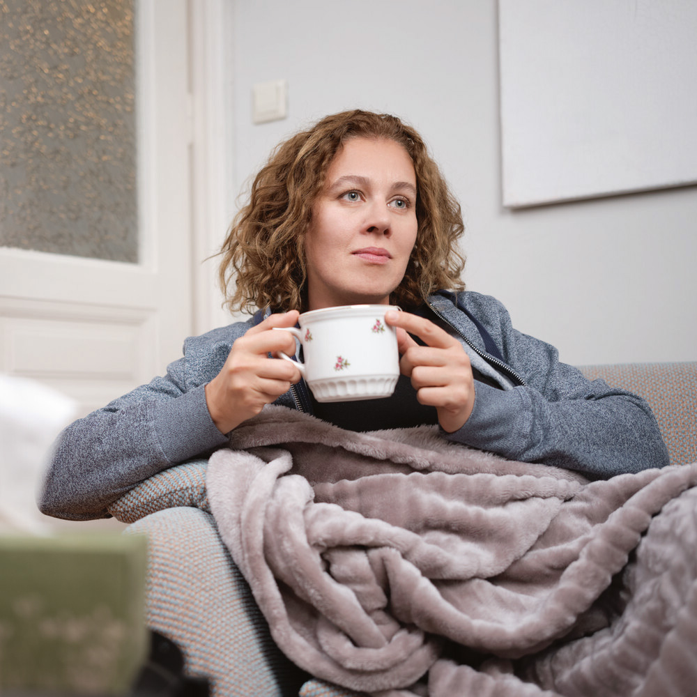 Frau mit Decke auf der Couch hält Teetasse. / Credit: ÖGK