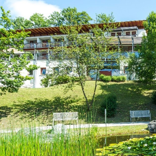 Außenansicht des Gesundheitszentrums Goldegg. Vor dem Gebäude sind eine Wiese, Bäume, ein Spazierweg, Bänke und ein Teich.