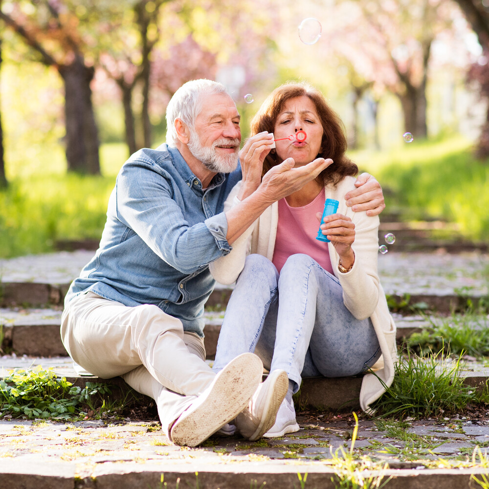 Älteres Paar sitzt im Park und macht Seifenblasen / Credit: Halfpoint/Shutterstock